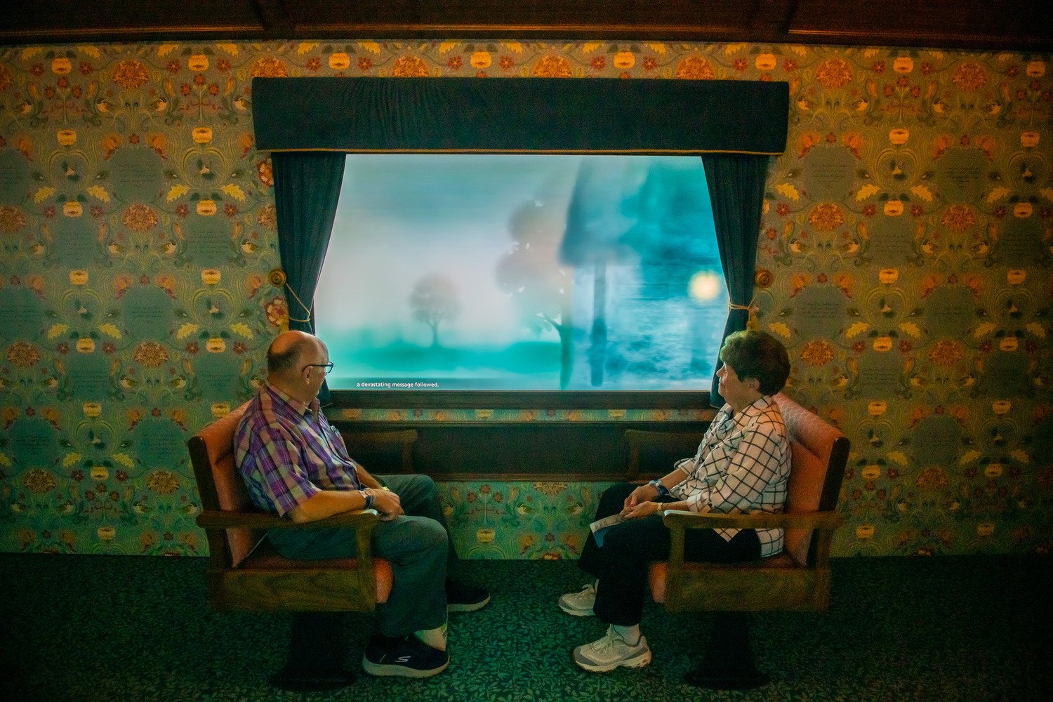 Two old people sitting down while looking out of window.