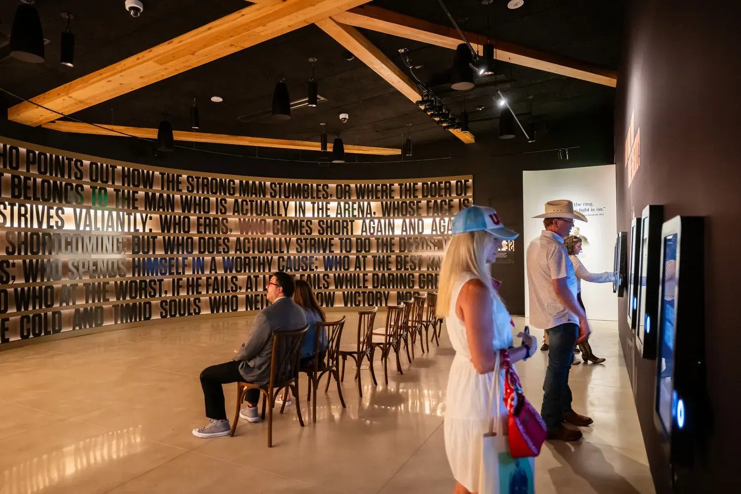 People viewing the 'In the Arena' exhibit while itneracting with the touch screens on the wall