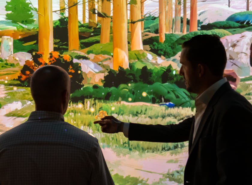 Two men facing the LED wall and one pointing toward the graphic.