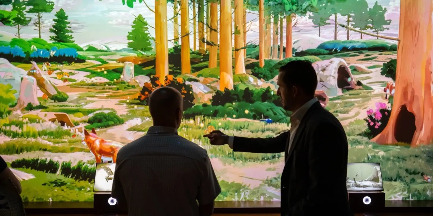 Two people pointing and interacting with the forest media on the wall.