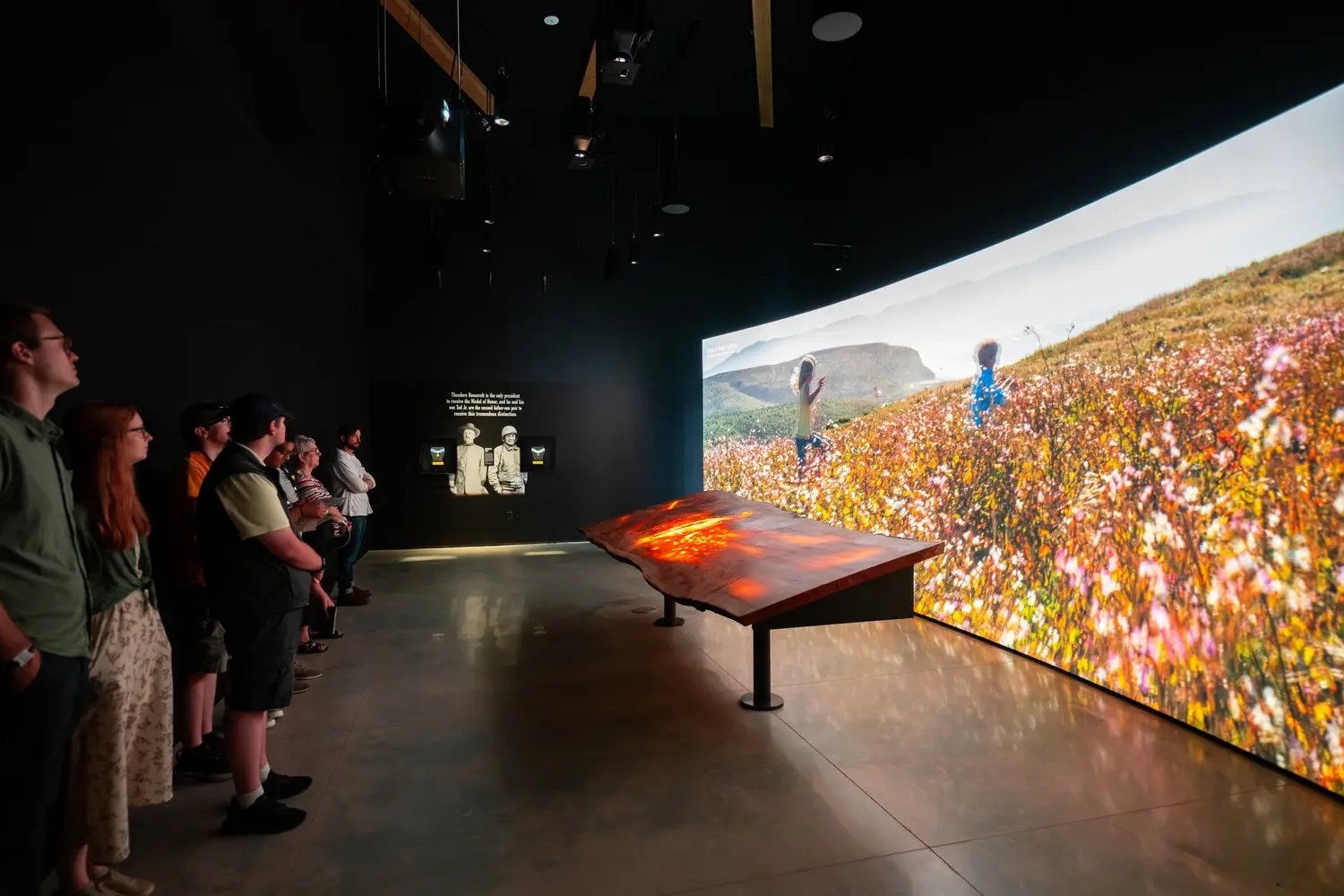 Group of people viewing curved wall with media.