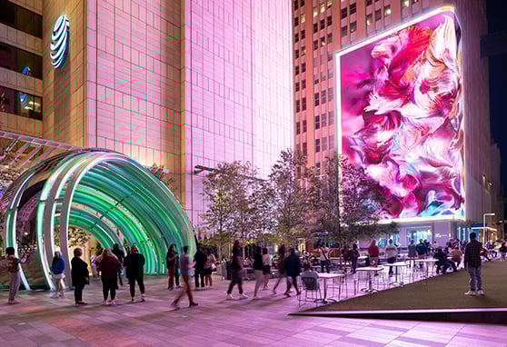 The vibrant AT&T Discovery District. The scene is anchored by a striking, oversized LED display with swirling pink and white visuals on the side of a tall building.