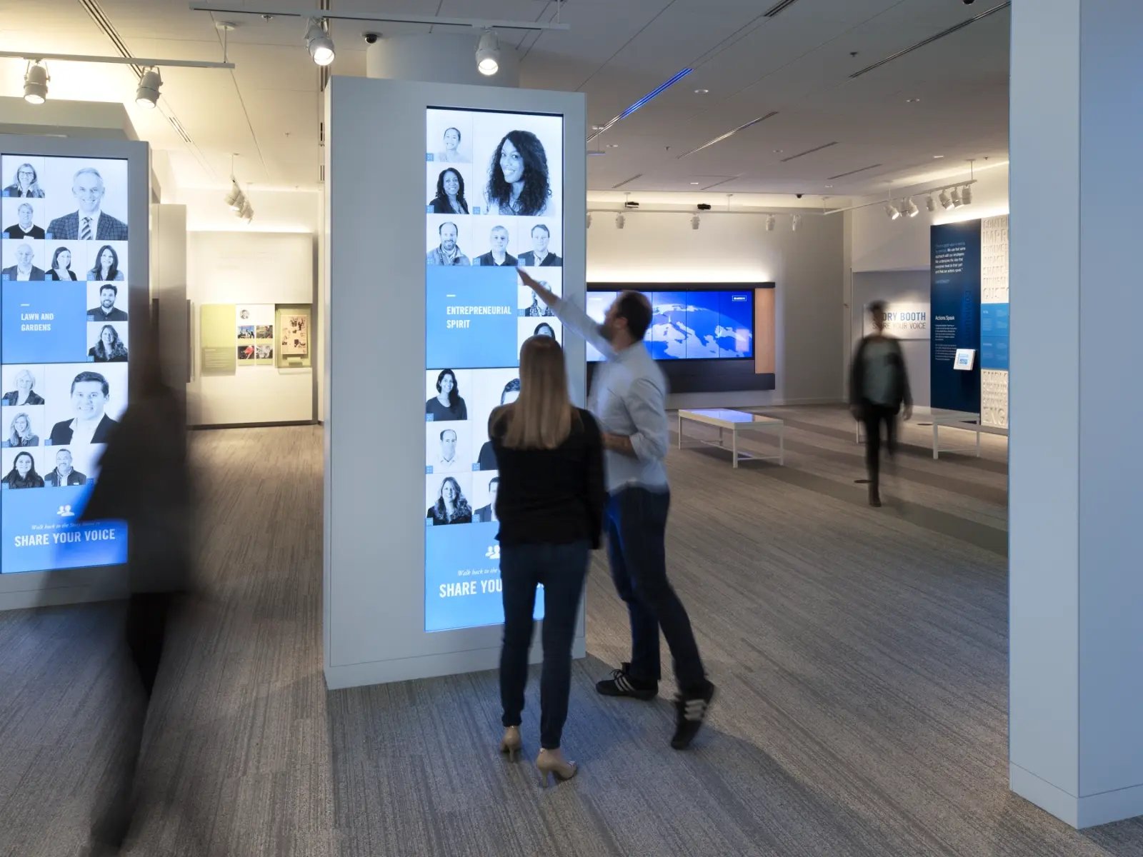 Two employees engaging with a large touch screen column.