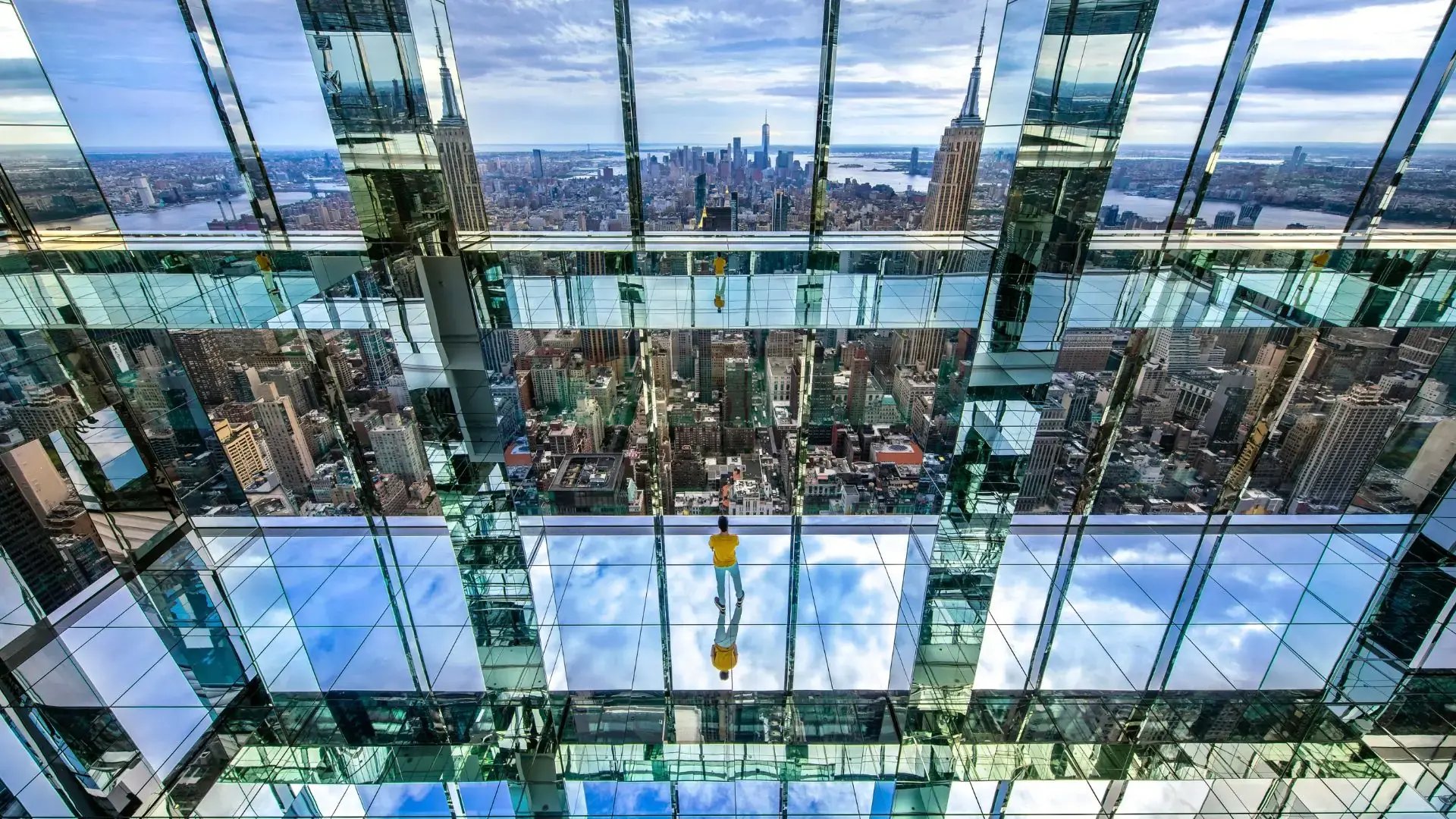 A visitor to the Summit One Vanderbilt observation deck experience standing in the mirrored room looking out to a view of the New York City skyline.