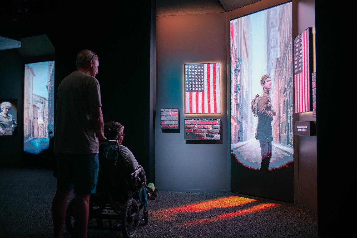 One person standing with the one in a wheelchair and both staring at the LED screen in front of them